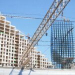 A train traveling past tall buildings under a blue sky